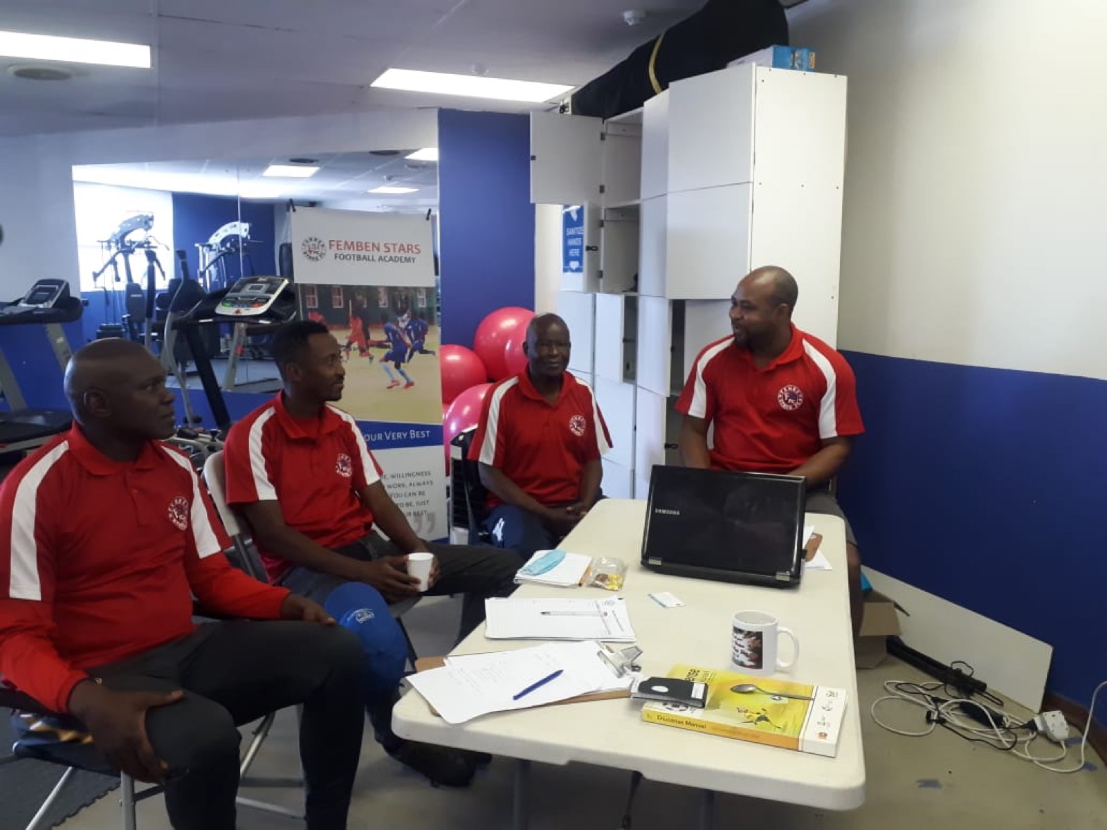 Femben academy team discussing football coaching around a laptop.